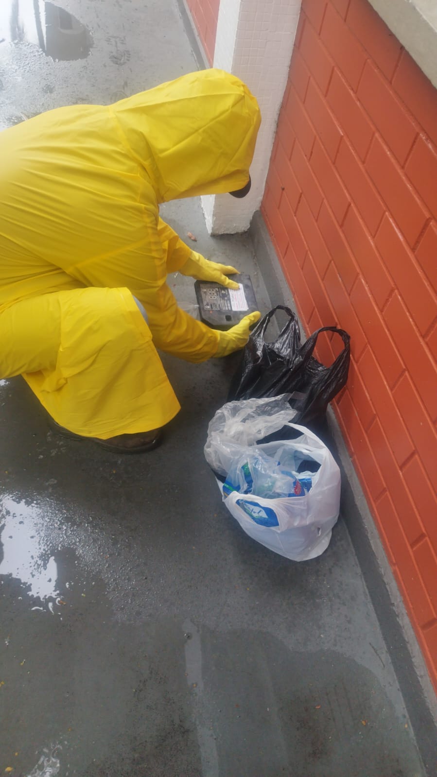 Técnico abrindo porta-isca com produto raticida ao lado de sacos de lixo